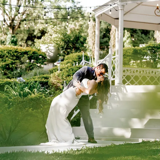Novios besándose sobre el prado con el gazebo al fondo