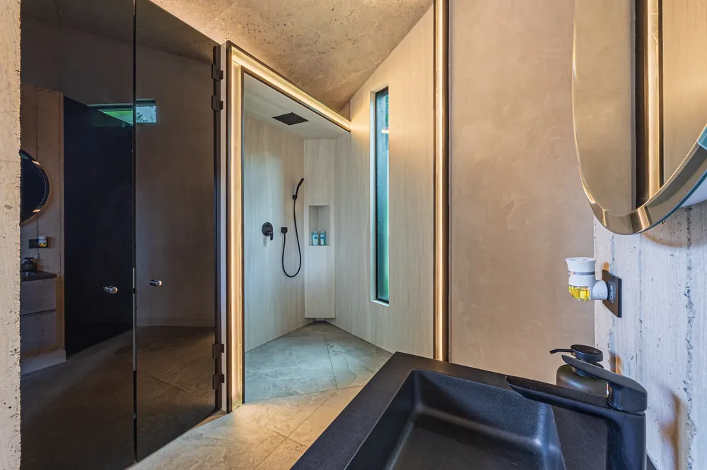 Baño de Nebulae con lavamanos negro de piedra y espejo circular sobre muro de concreto