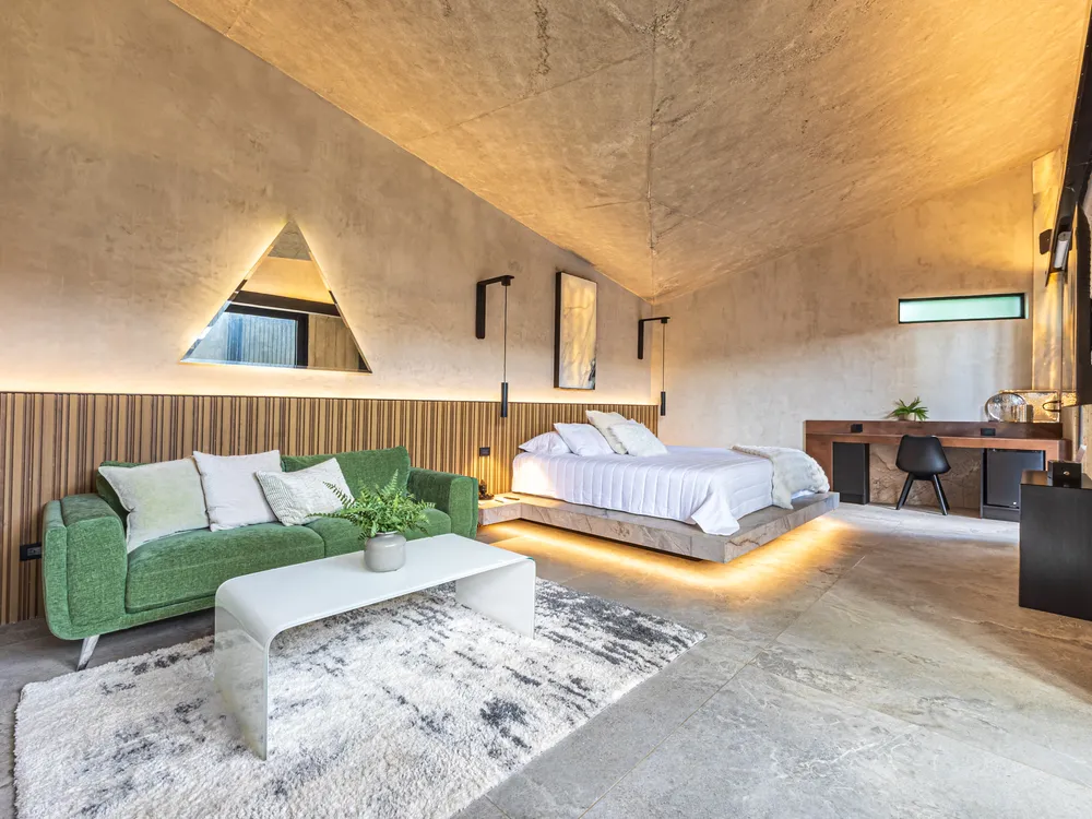 Habitación de Nebulae con cama iluminada por luz indirecta, techo de concreto y ventanal al jardín