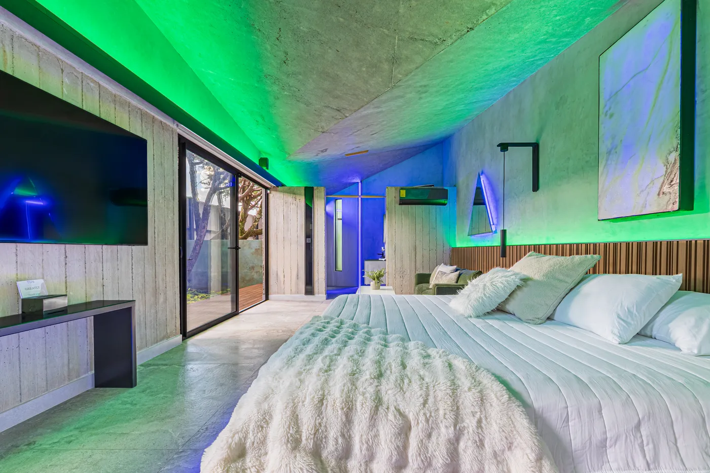 Habitación de Nebulae con la cama bajo luz LED verde y azul sobre el techo de concreto