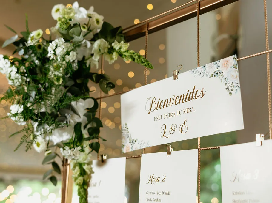 Rótulo de bienvenida con el plano de mesas, decorado con flores blancas y follaje