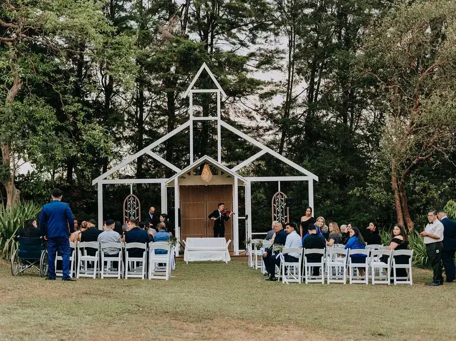 Fachada estilo iglesia de estructura blanca sobre el prado de Laureal, con sillas dispuestas para la ceremonia y el bosque detrás