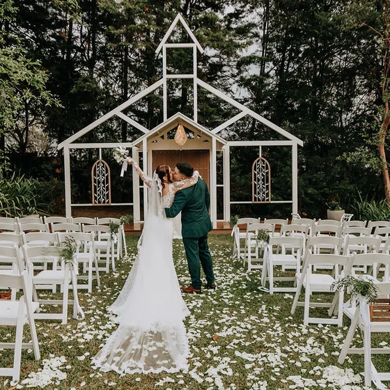 Novios frente al altar de la Fachada de la Iglesia, rodeados de sillas blancas y pétalos