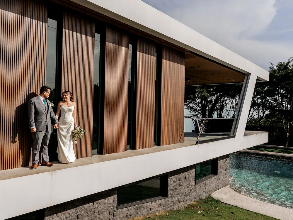 Novios junto a la fachada de listones de madera de Nebulae, sobre la piscina