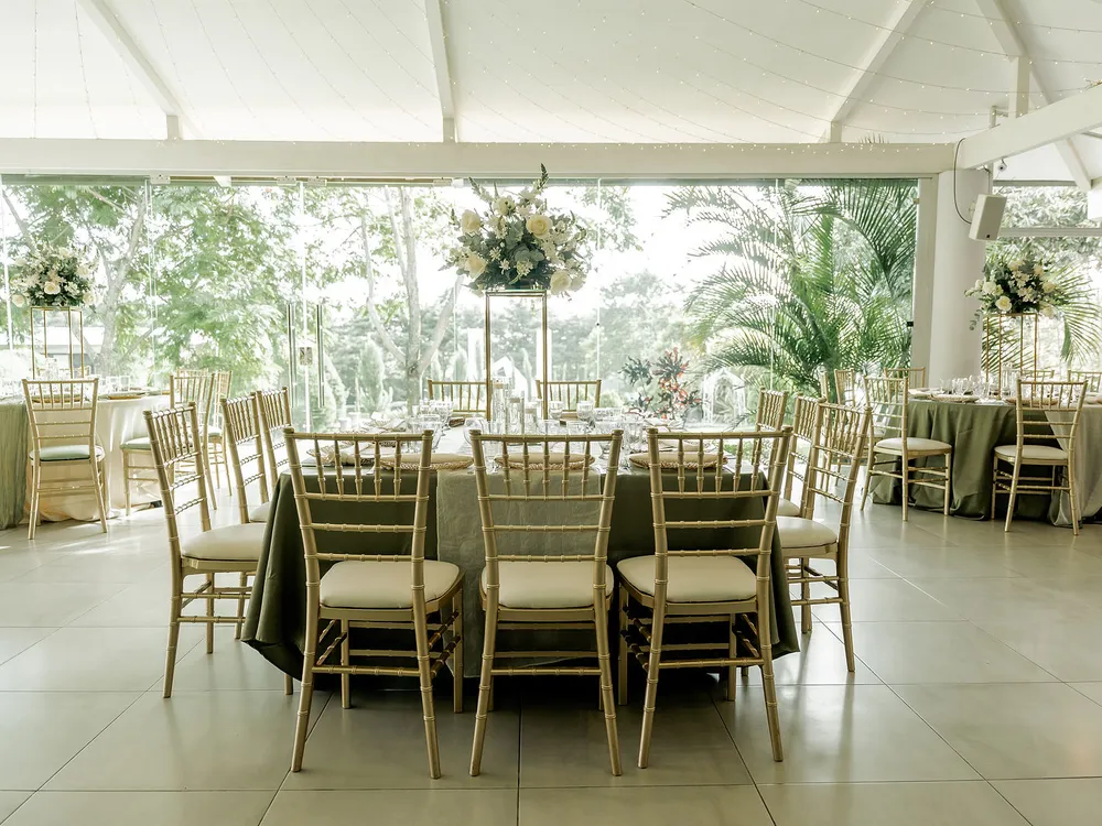 Salón principal de Laureal montado de día con mesas, mantelería verde salvia y sillas tiffany, abierto hacia el jardín