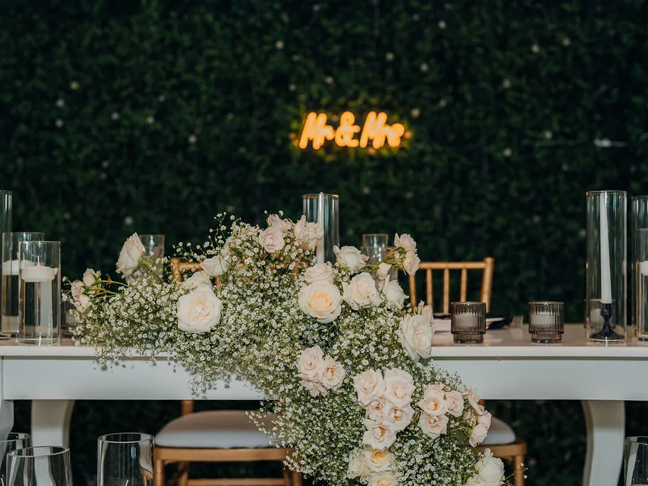Mesa principal decorada con arreglo floral y rótulo de neón sobre el muro verde del salón