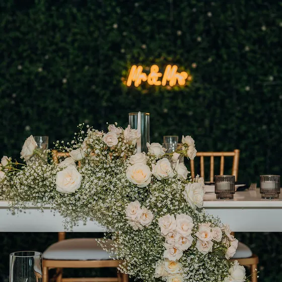 Mesa principal con arreglo floral y rótulo de neón sobre el muro verde