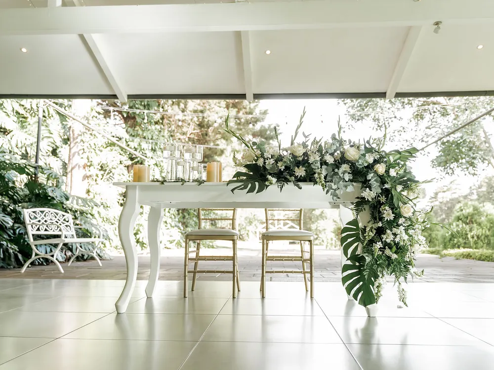 Mesa principal de los novios con arco floral blanco y vista al jardín